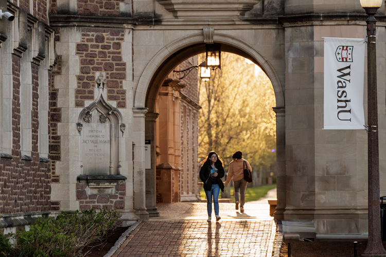 Students walking through building archway on campus on sunny day
